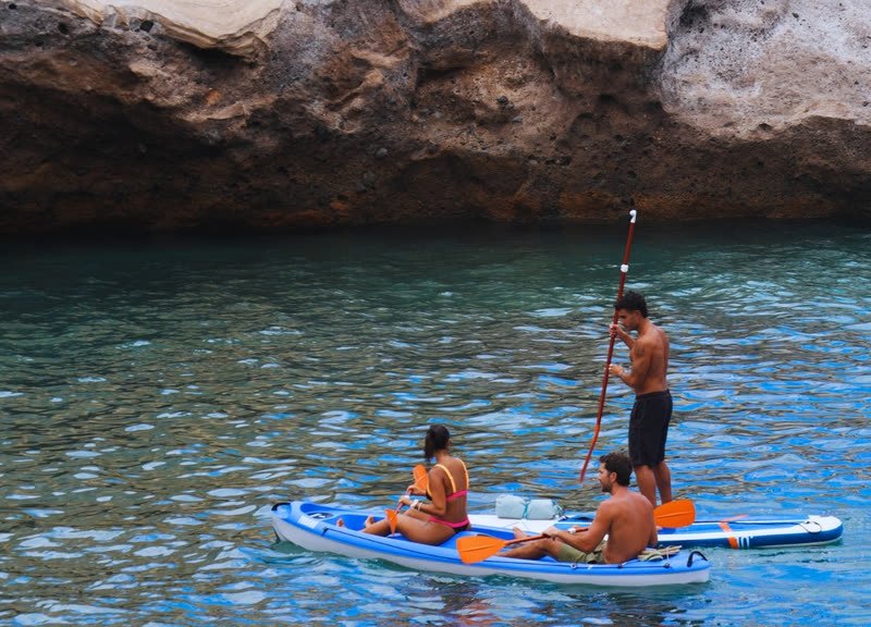 Un chico de pie en su tabla de paddle surf y una pareja en kayak junto al acantilado