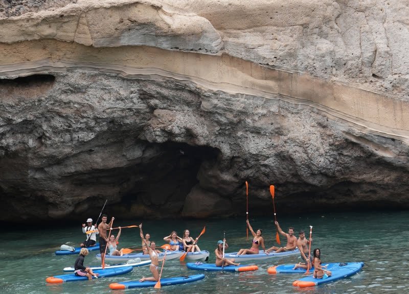 Grupo de paddle surf y kayak levantando las palas frente al acantilado